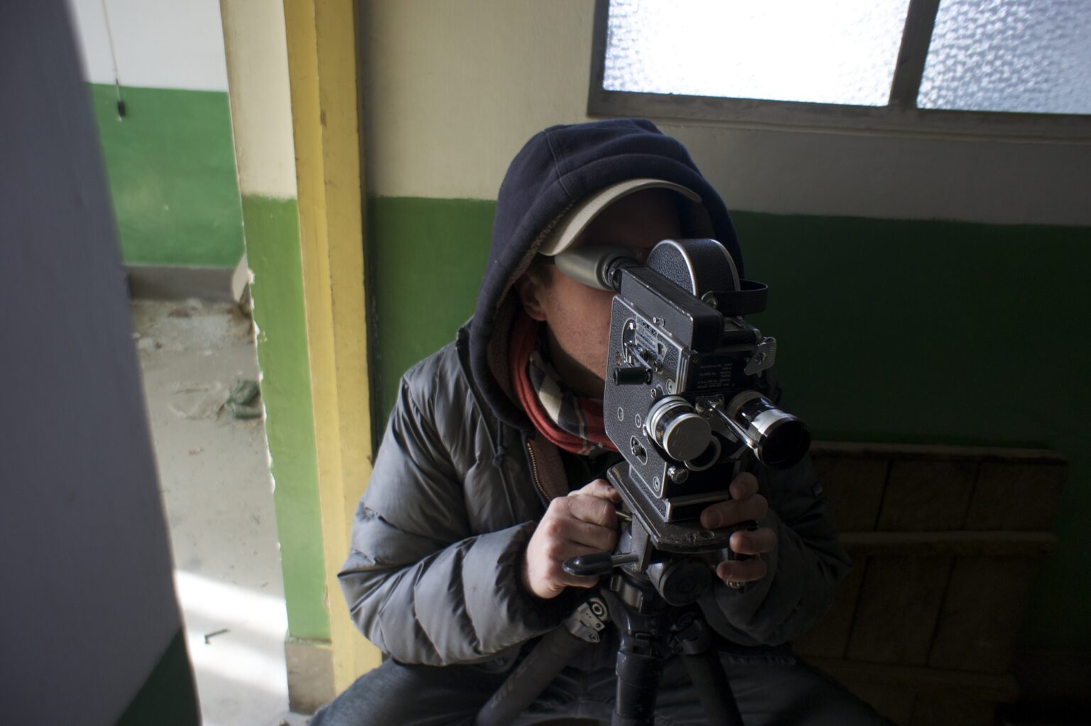 A person crouching behind a film video camera.