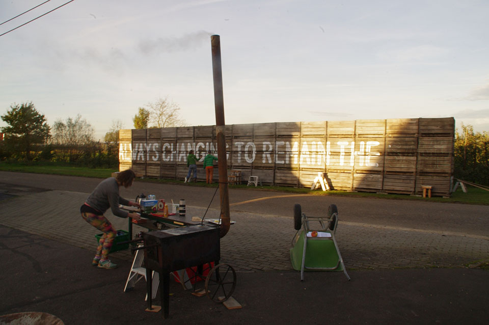 A photographe of people painting a mural and a person working at a table near a portable stove.