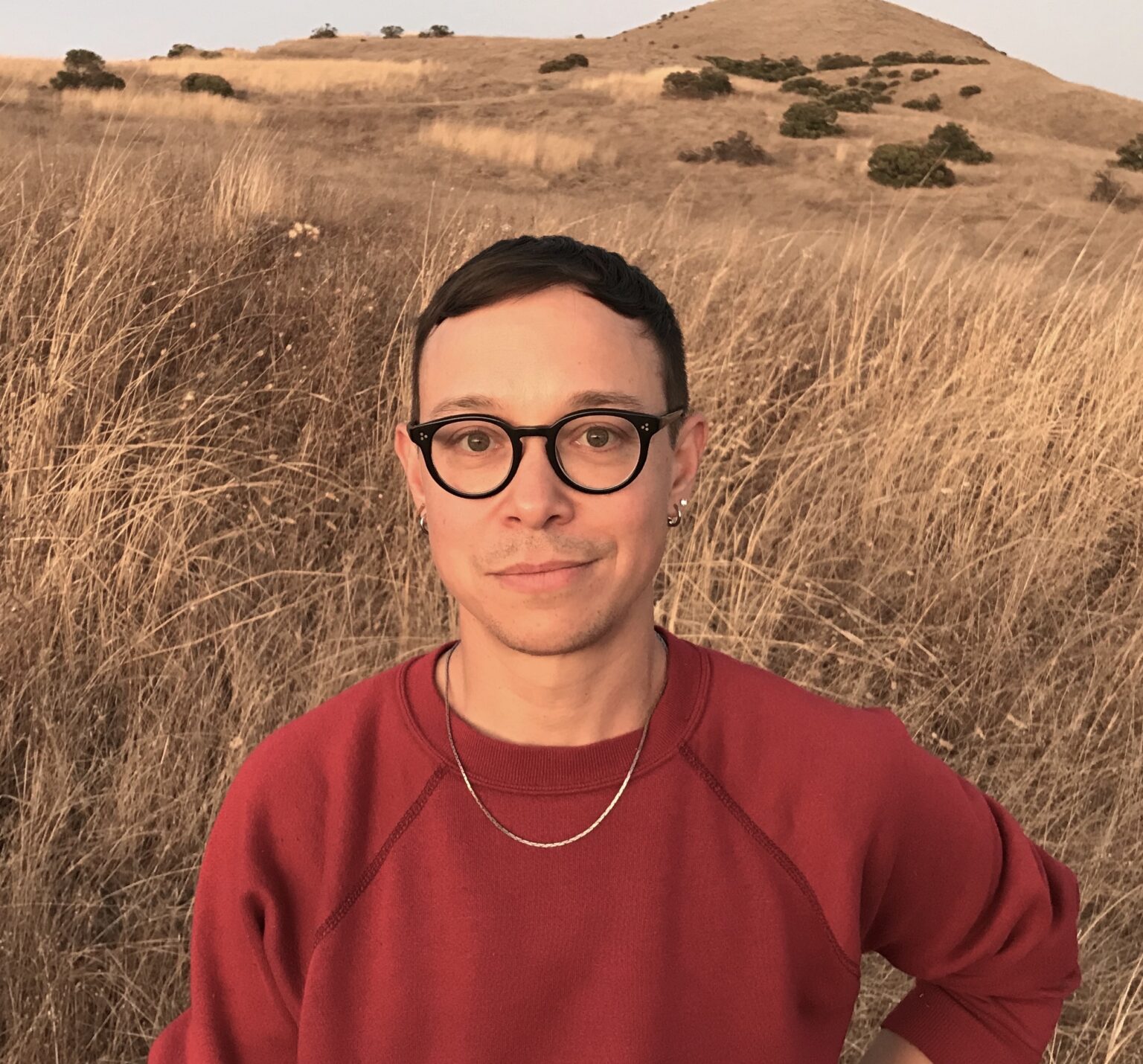 A portrait of a person in front of a field and hills.