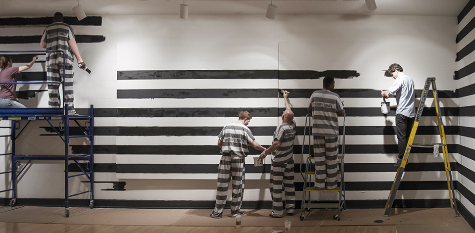 A group of people painting black stripes onto a white wall.
