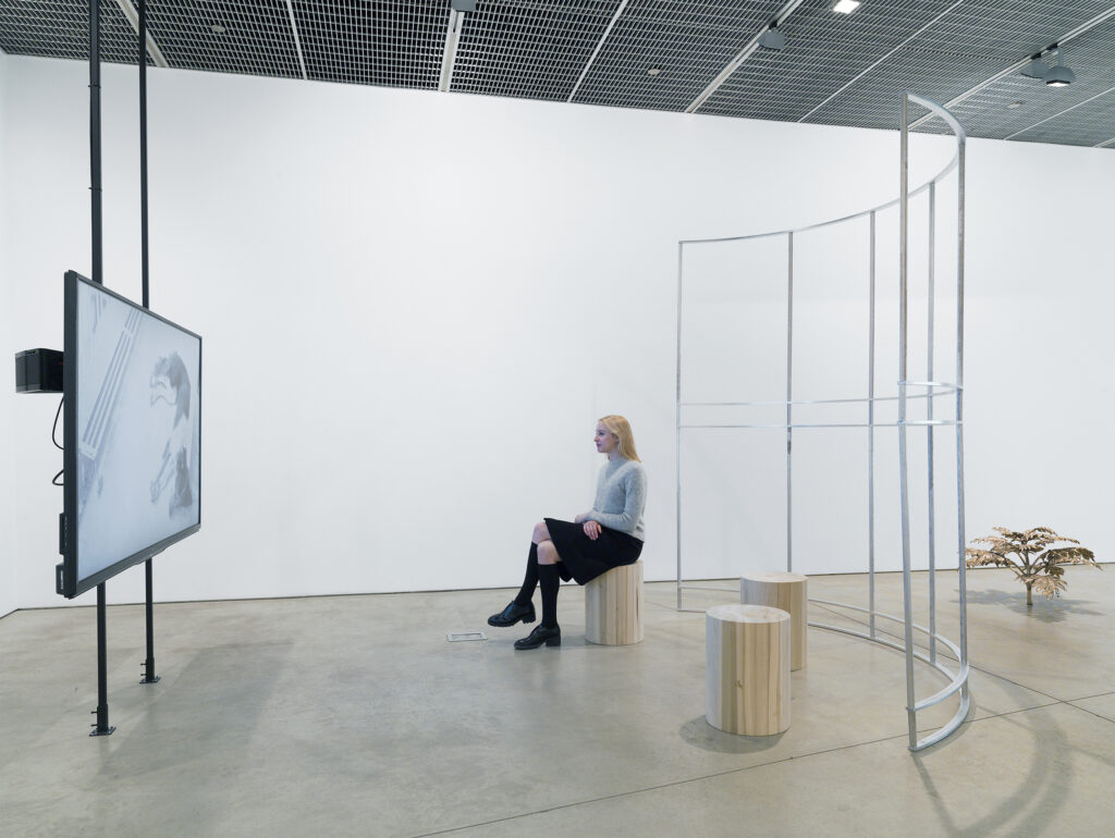 A person sitting in a gallery watching a flat screen television.