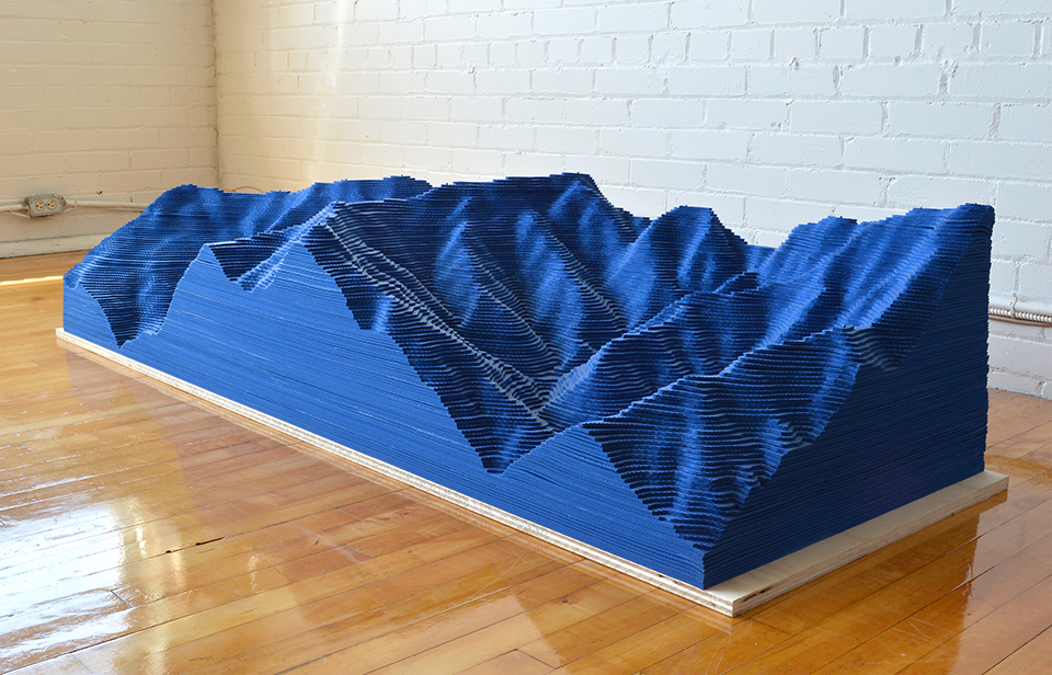 A blue, mountainous installation in a gallery.