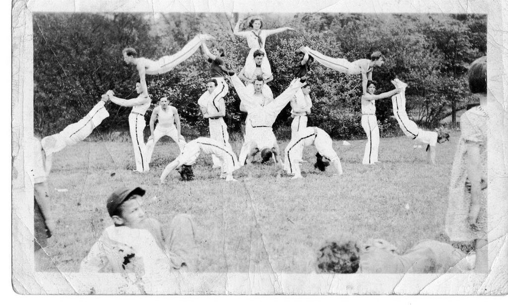 A group of people in uniforms creating an acrobatic formation outside.
