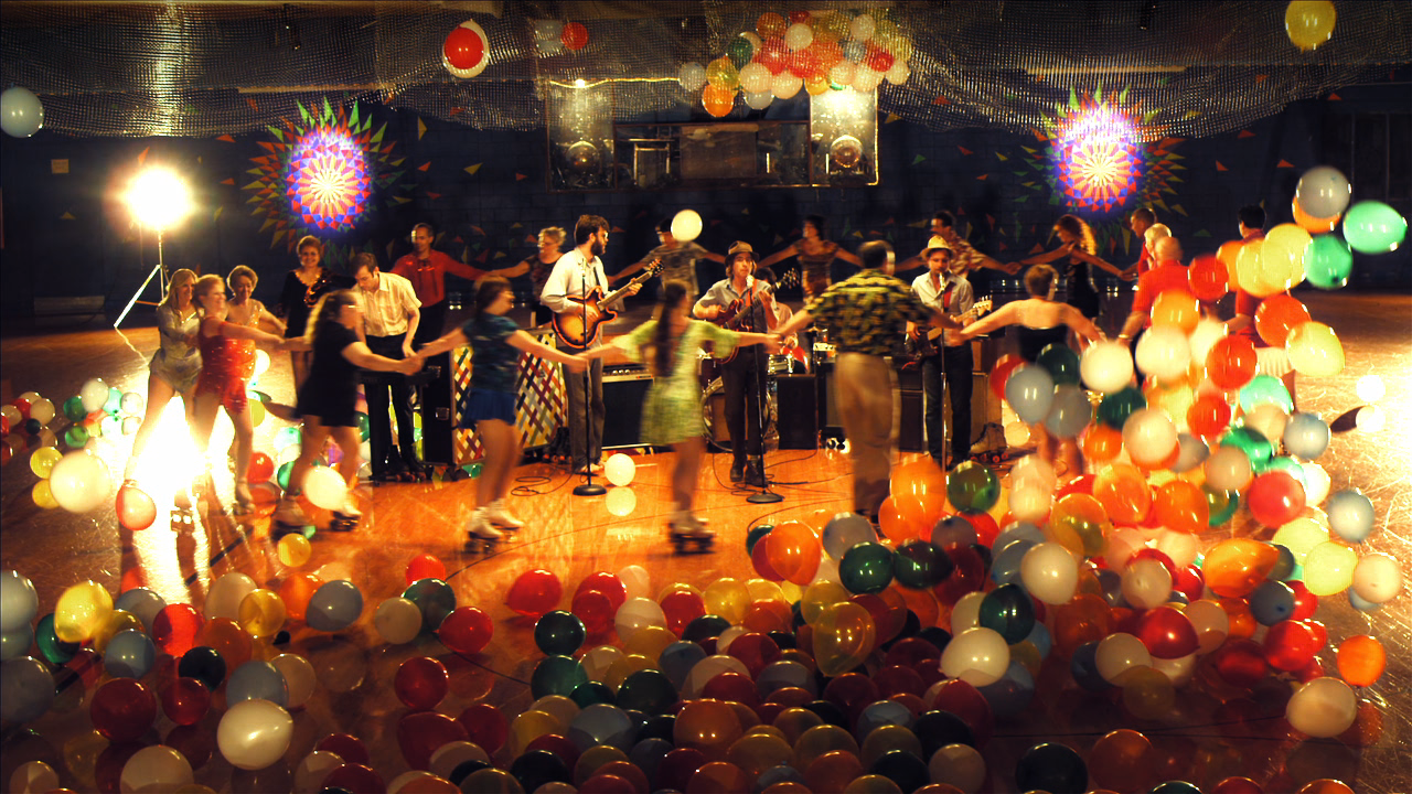 A rock band enriched by roller skaters and balloons.