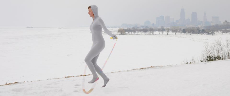 A person skipping rope in the snow with a city skyline in the background.