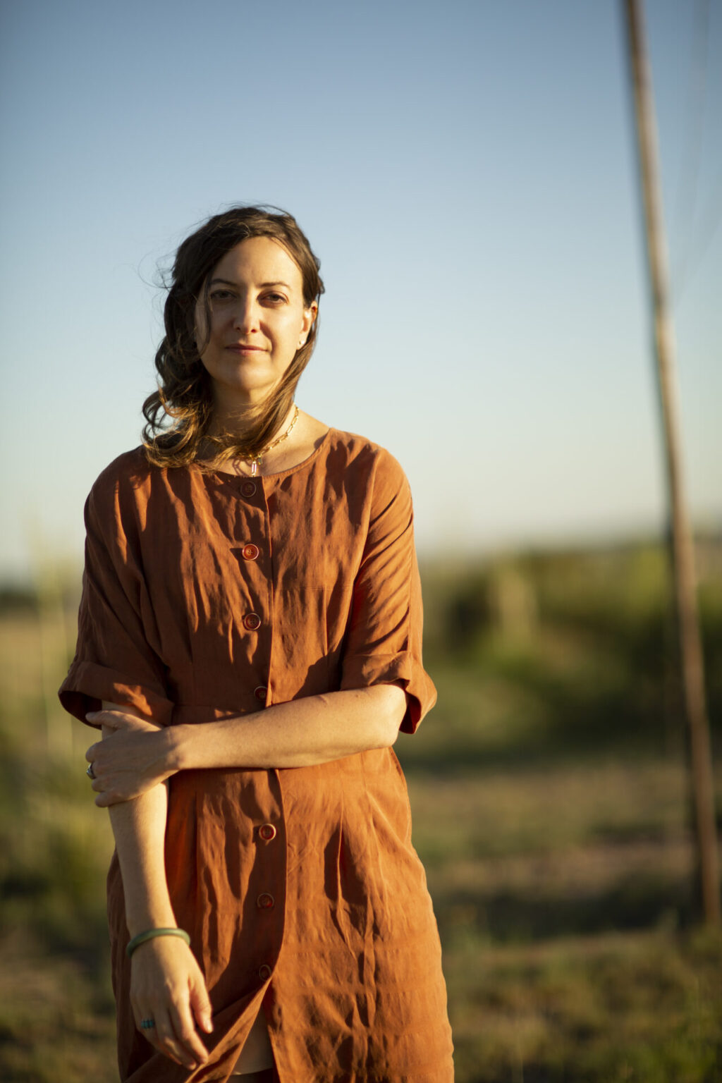 The artist in orange dress standing in front of a landscape.