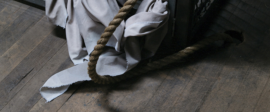 A close-up image of a rope, wooden floor, and light-coloured fabric.