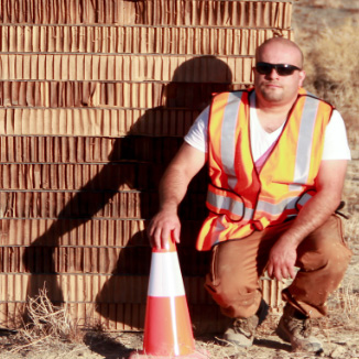 A person kneeling by a traffic cone in front of a brick wall.