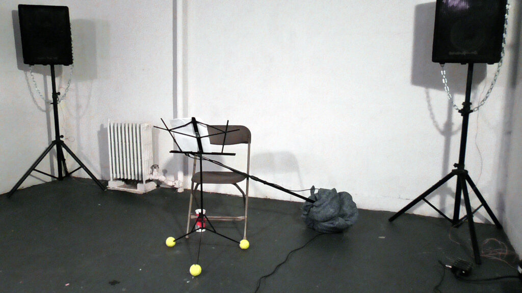 A music stand, chair, and speakers set up in a room.