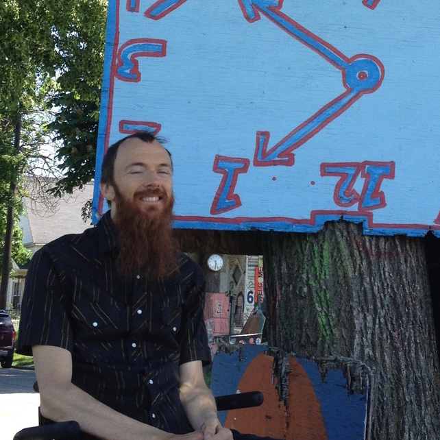 A person sitting outside in front of a painted clock.