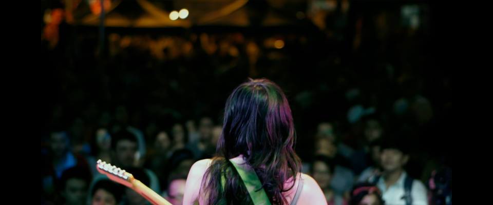 The back of a person playing guitar with an audience in the background.