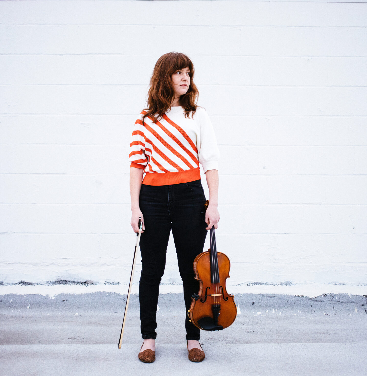 A person standing and holding a violin in one hand and a bow in the other.