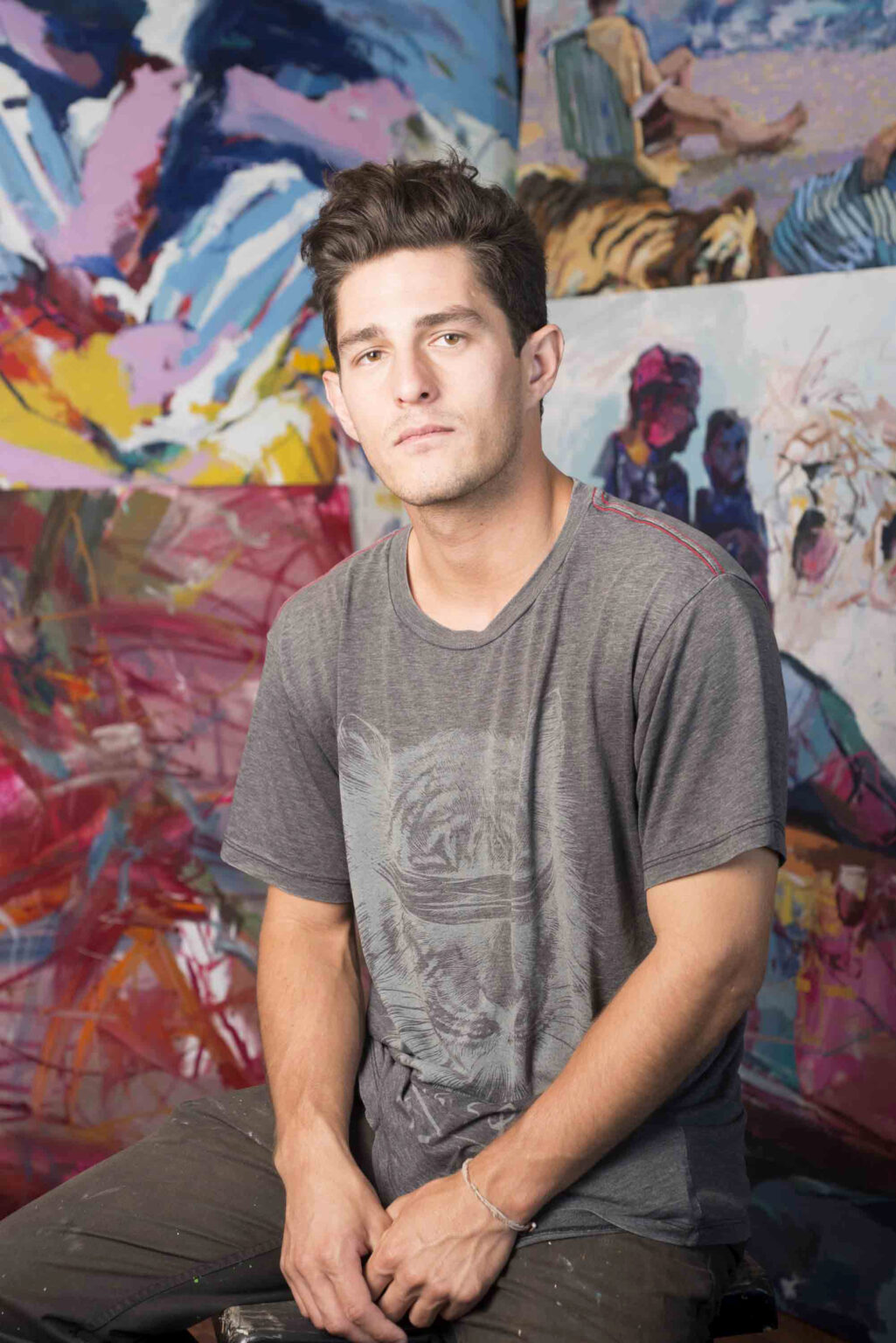 A portrait of a person sitting in front of paintings.