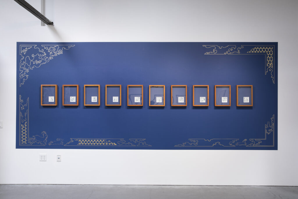 A series of ten artworks mounted onto a blue and gold painted wall.