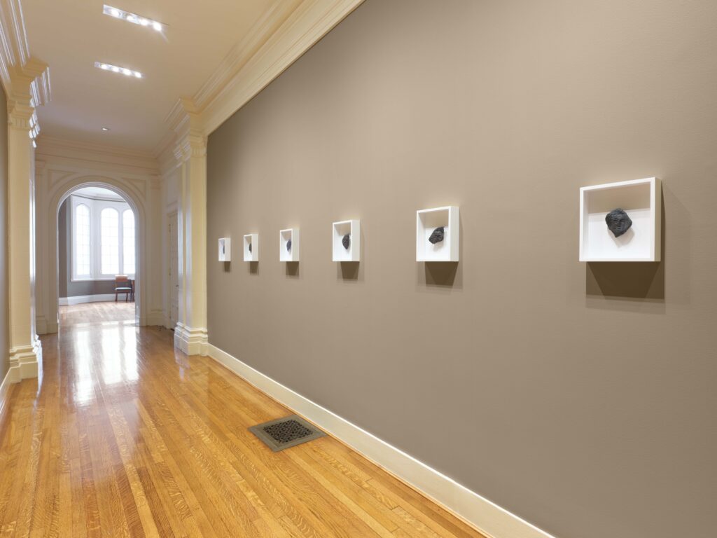 Photo of a long wall with a series of small framed black objects in white frames.