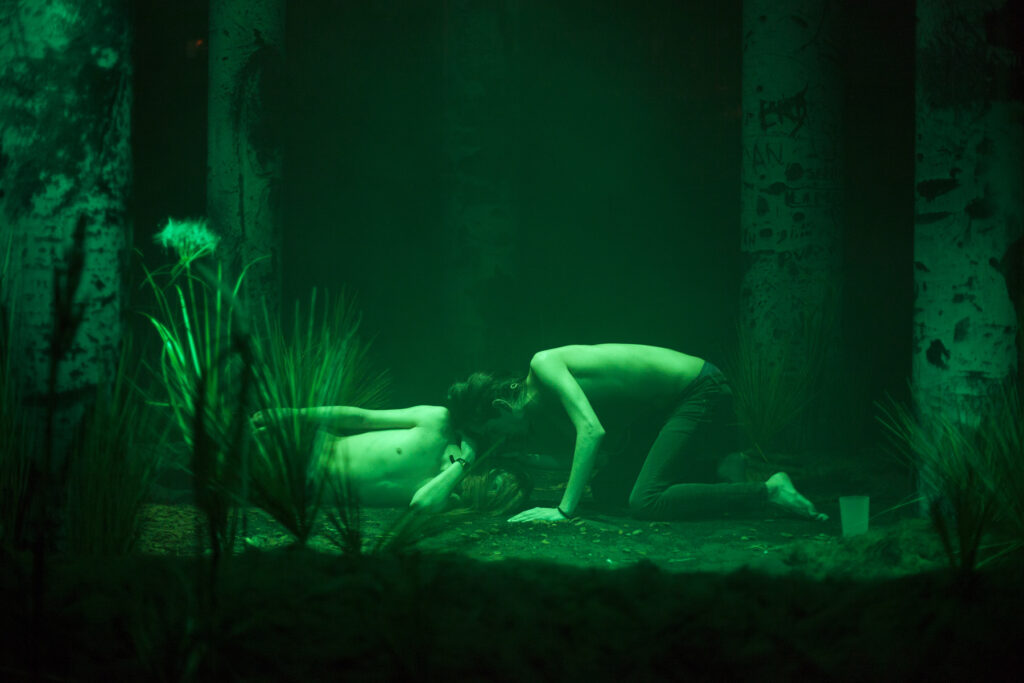Two people in a forest scene lit by a green light.