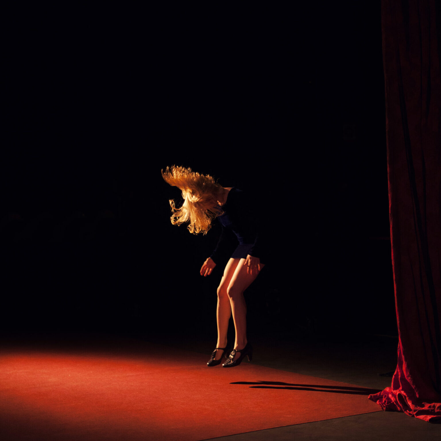A person jumping in a shadowed room and lit by a red light.