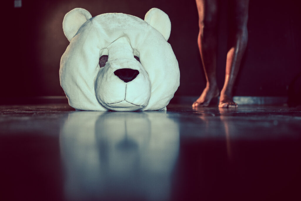 A person's legs next to a large stuffed bear head.