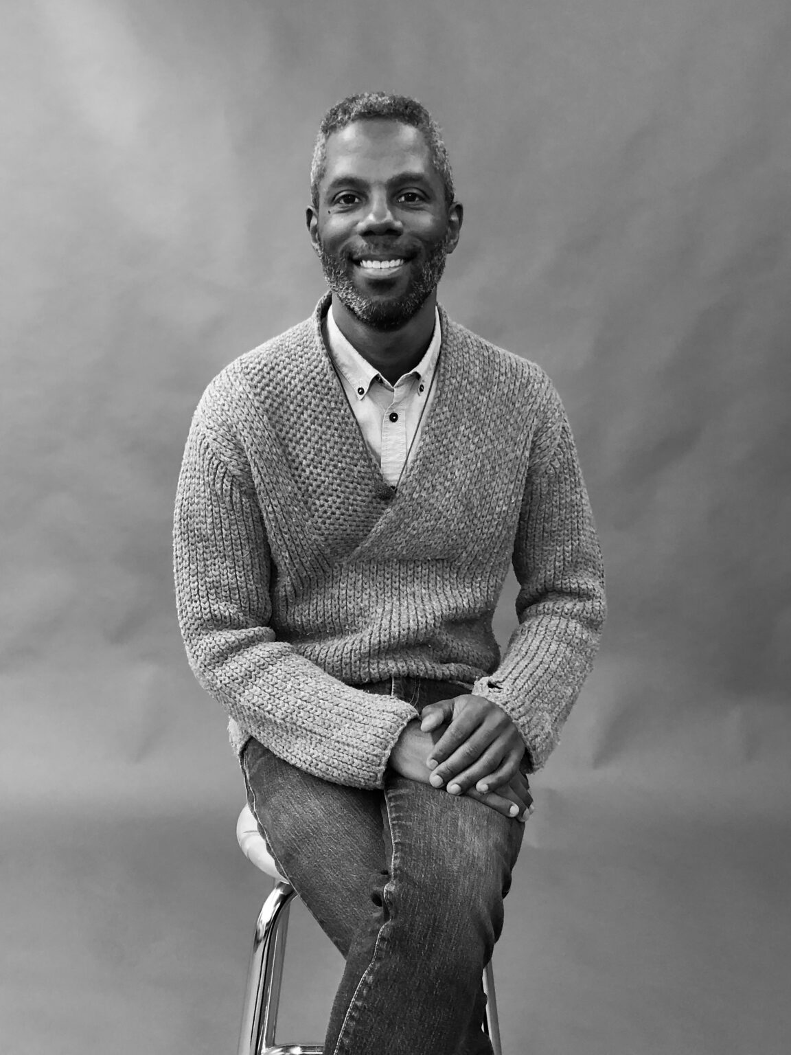 A portrait of a person sitting on a stool.
