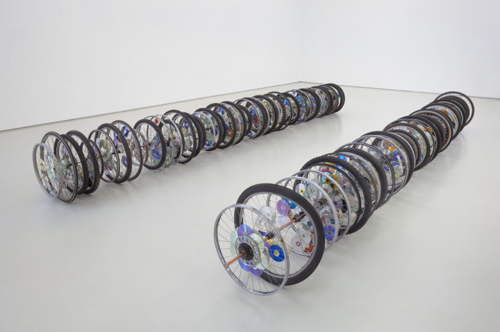 An installation of two rows of bicycle rims and wheels in an art gallery.