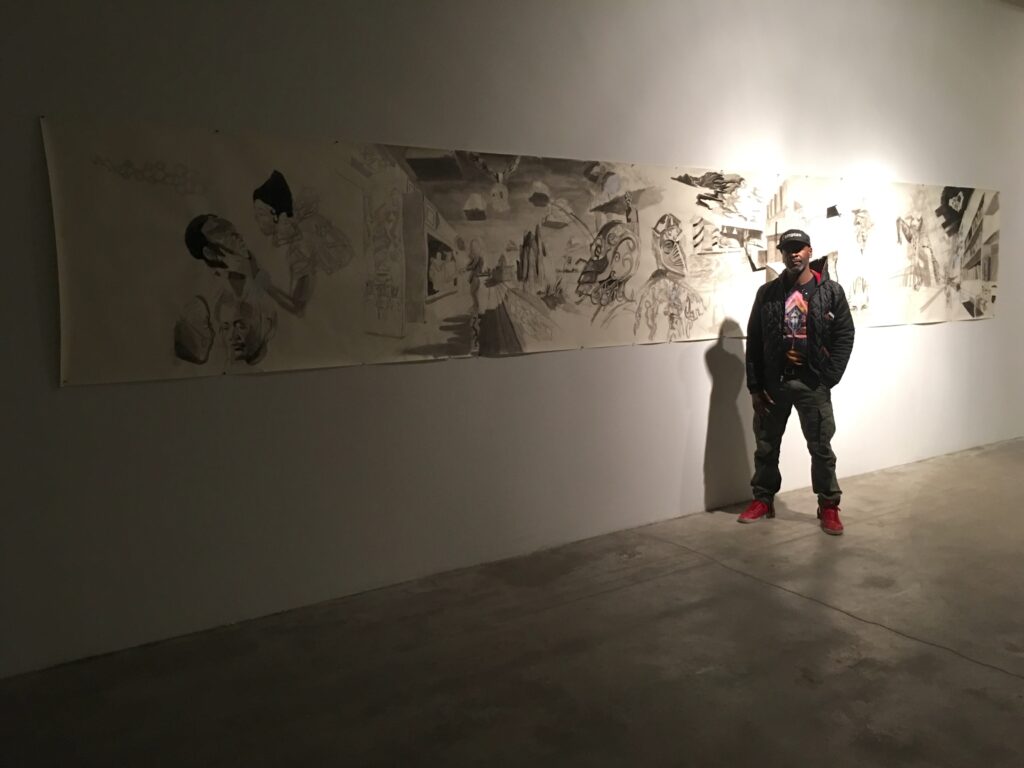 A person standing in front of a long work on paper mounted to a gallery wall.