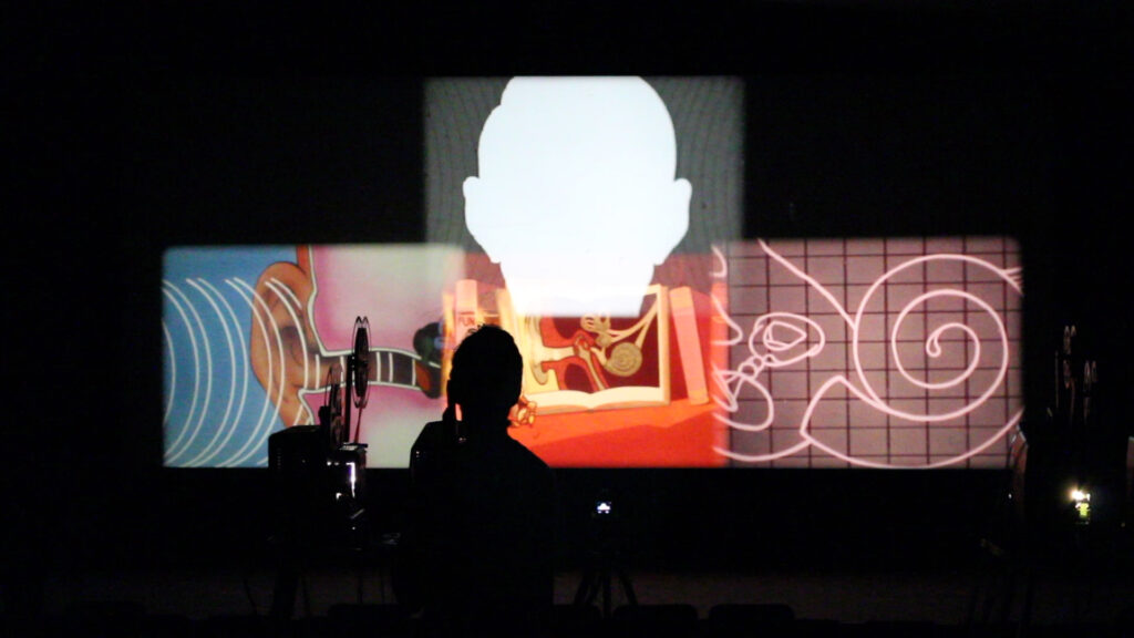 A silhouette of a person and a projector with colorful images projected behind.