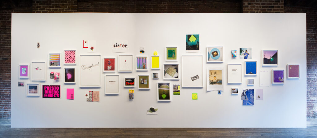 A group of multi-colored framed works hung on a white wall.