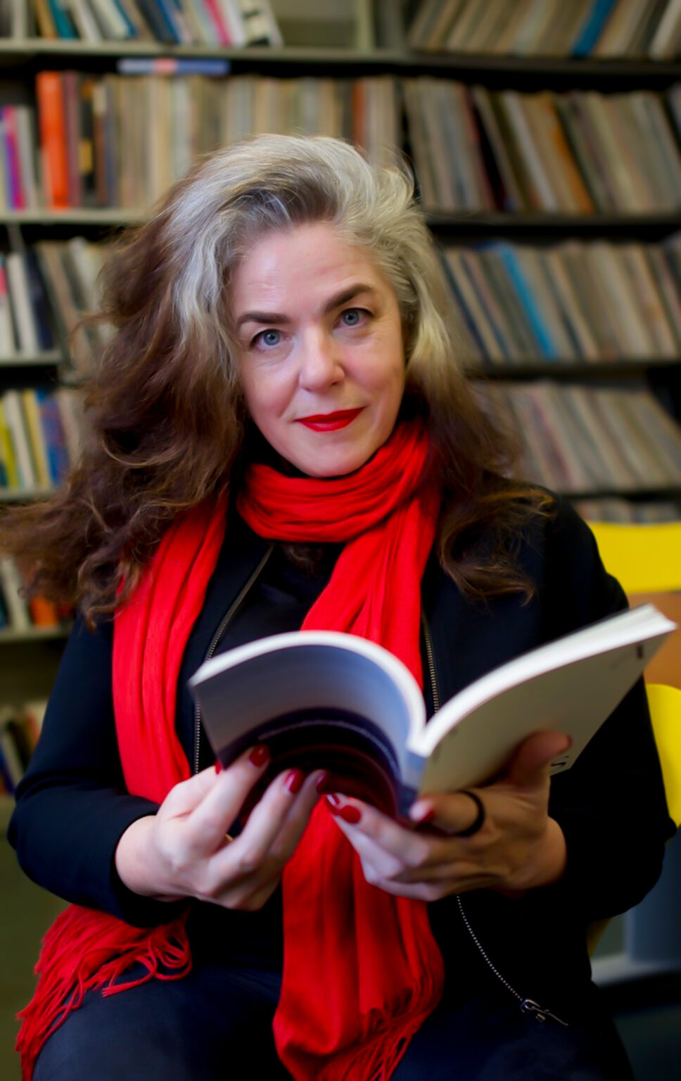 A person holding a book in front of a bookshelf.