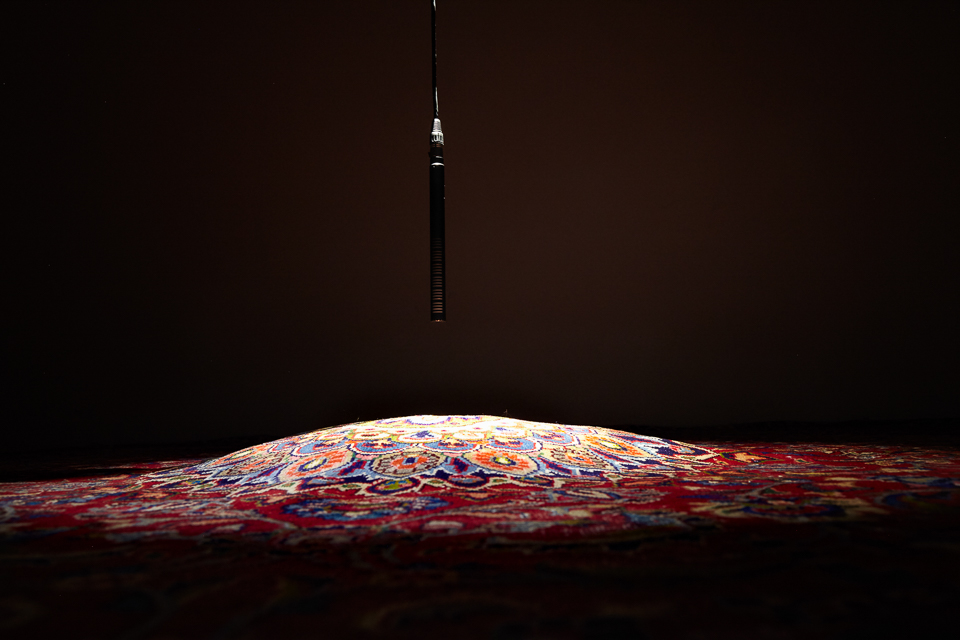 An image of an art installation comprised of a patterned rug and hanging microphone.