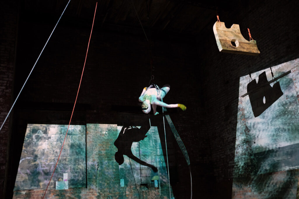 A dramatically lit set with a person hanging from ropes
