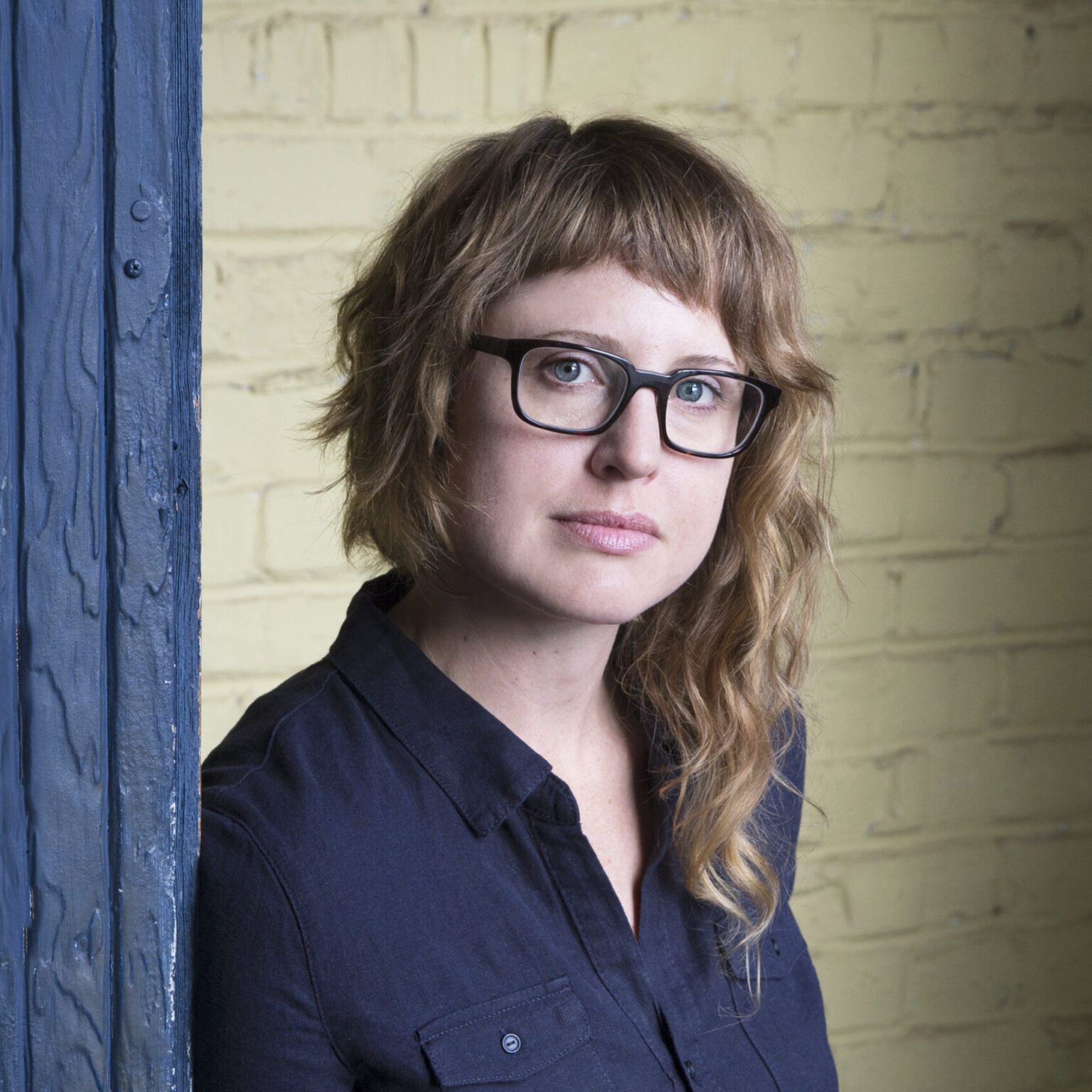 A portrait of a person leaning against a painted wood and brick structure.