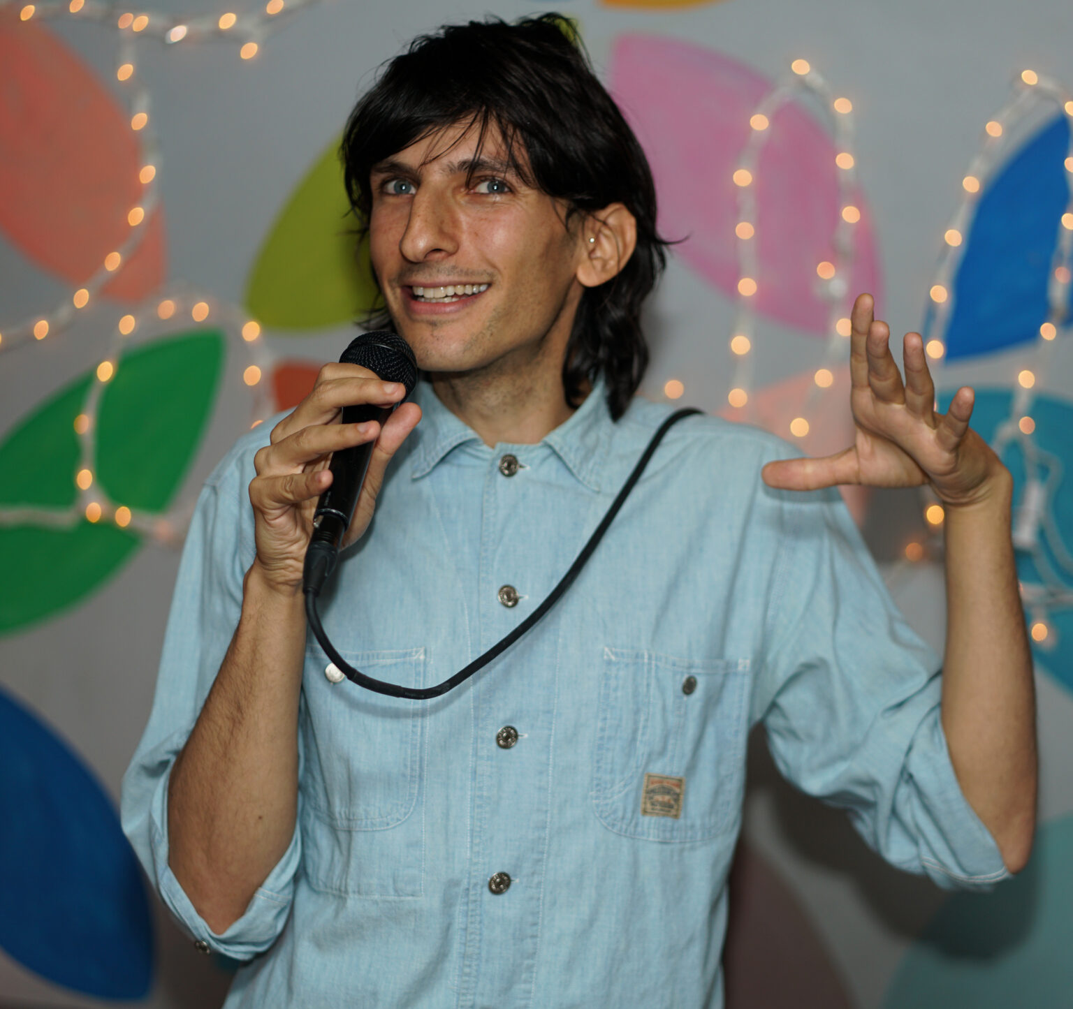 A person holding a microphone in front of a must-colored background.