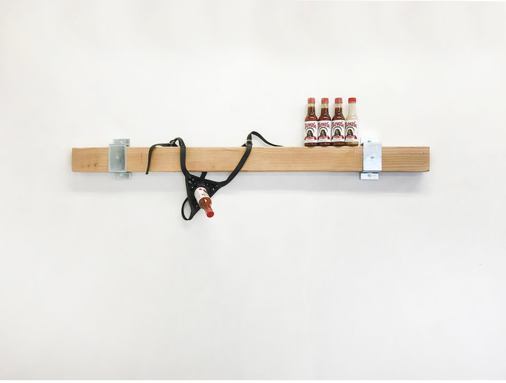 A shelf with bottles of Tapatio and a strap-on.