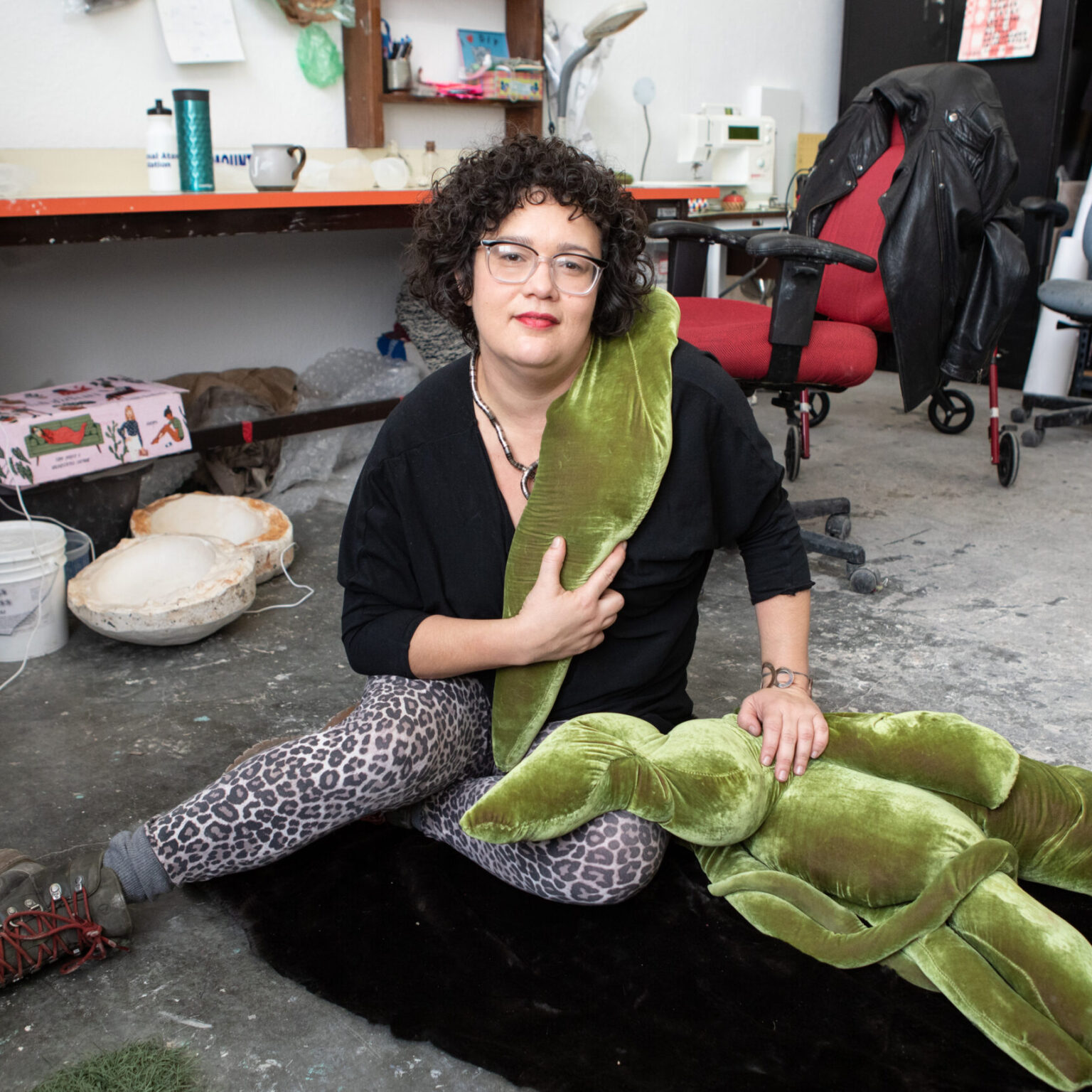 A person sitting in a workshop with a soft sculpture.