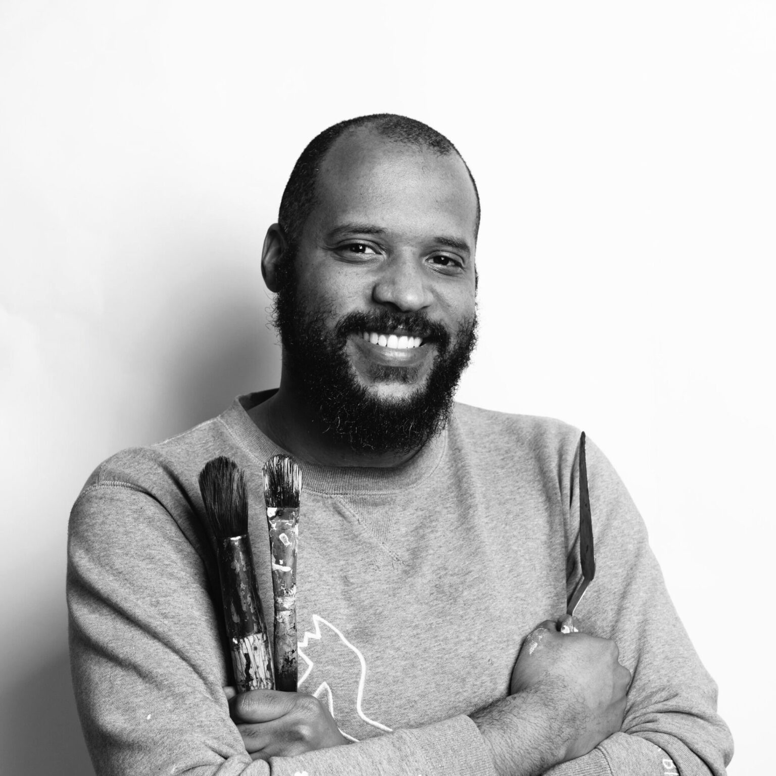A person holding paintbrushes and standing against a white backdrop.