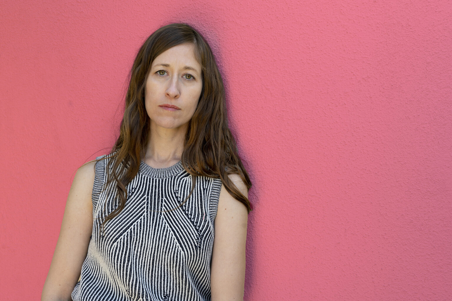 A portrait of a person against a pink background.