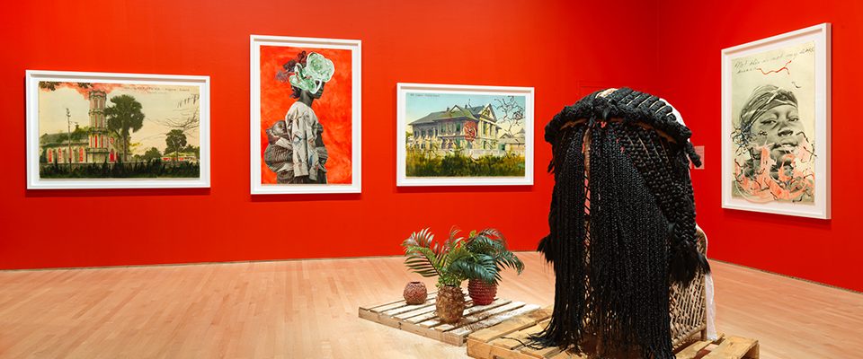 Art gallery with red walls, artworks hanging on walls, and artworks displayed on showroom floor.