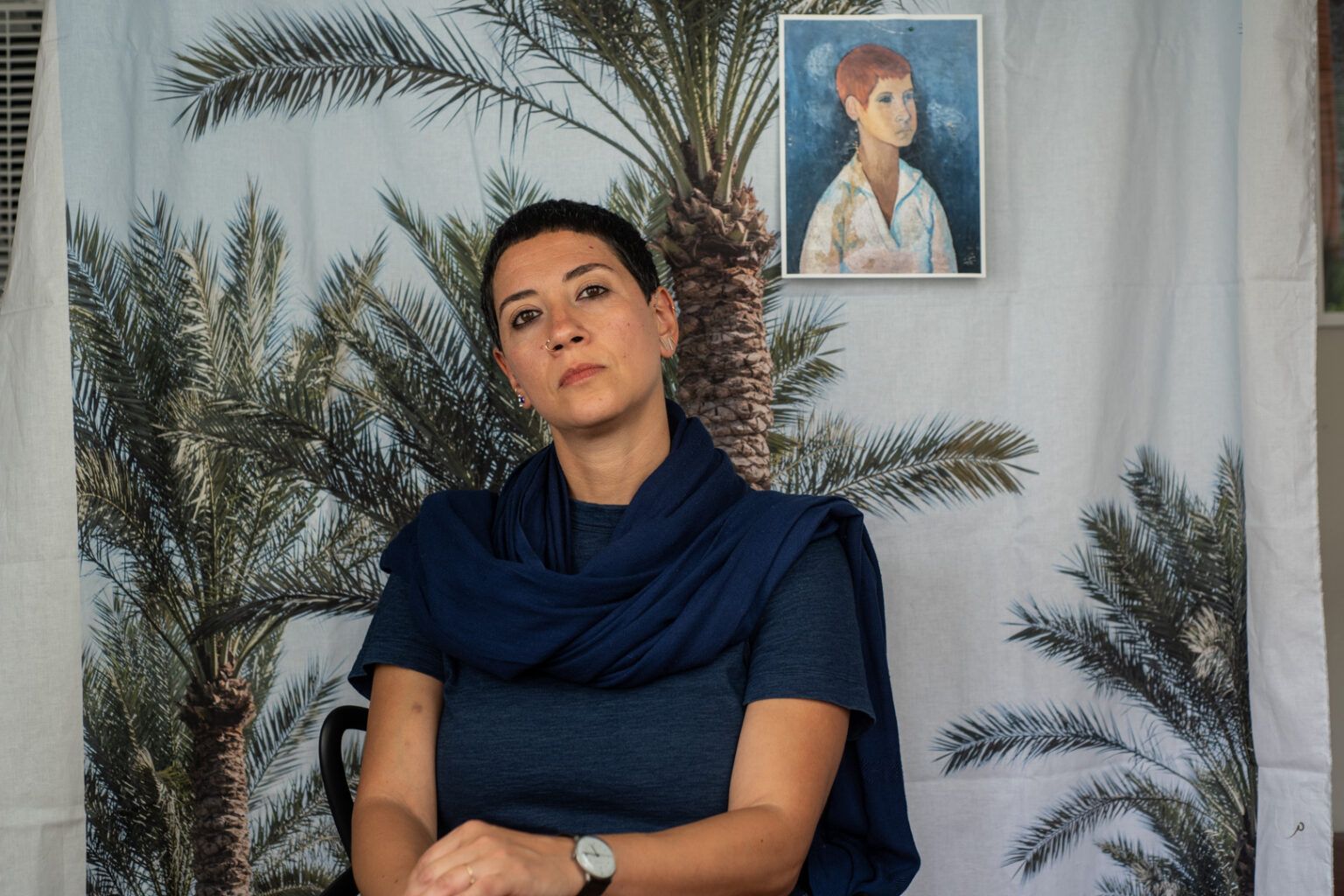 Person sitting in front of cloth backdrop printed with palm trees.