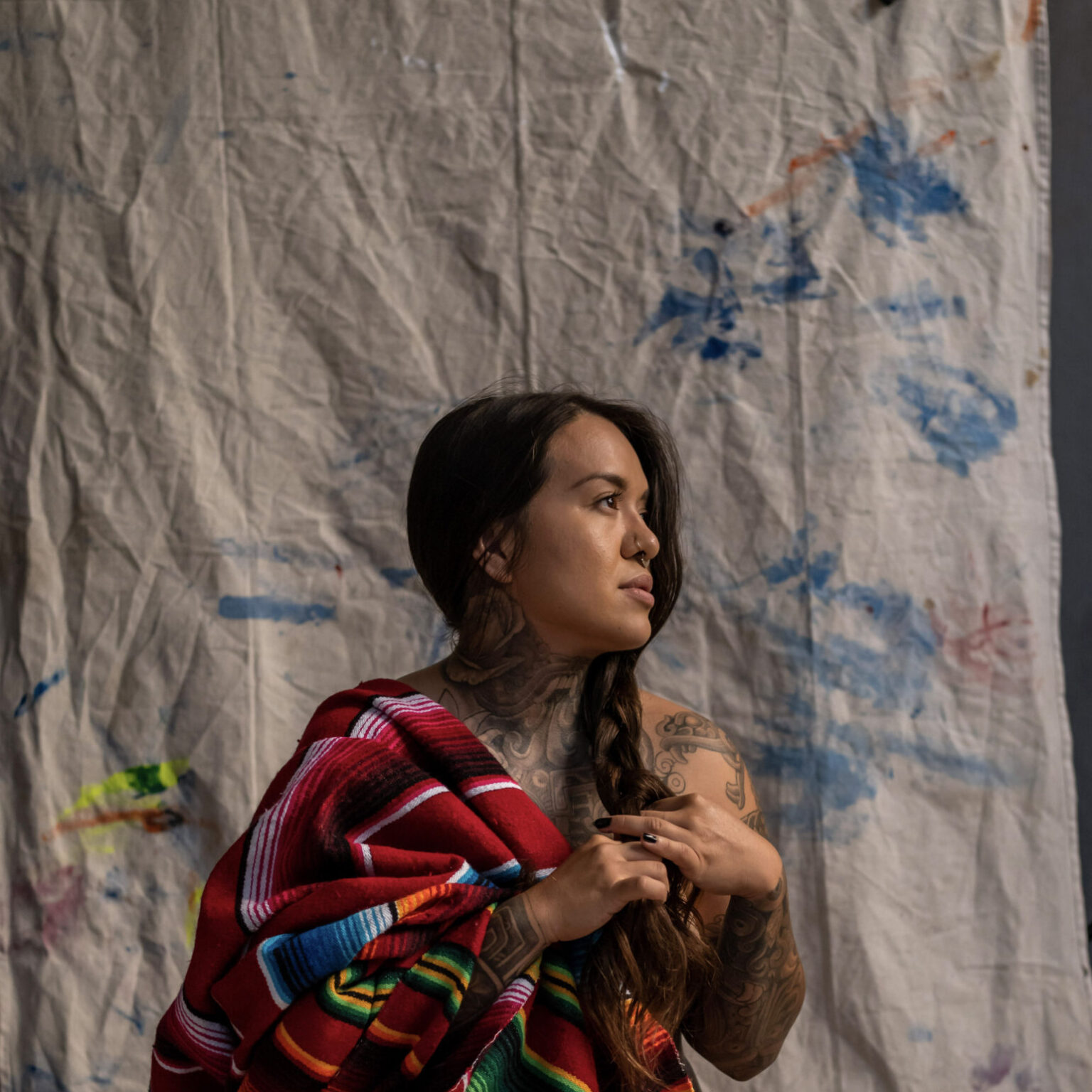 Person sitting on drop cloth and draped in blanket.