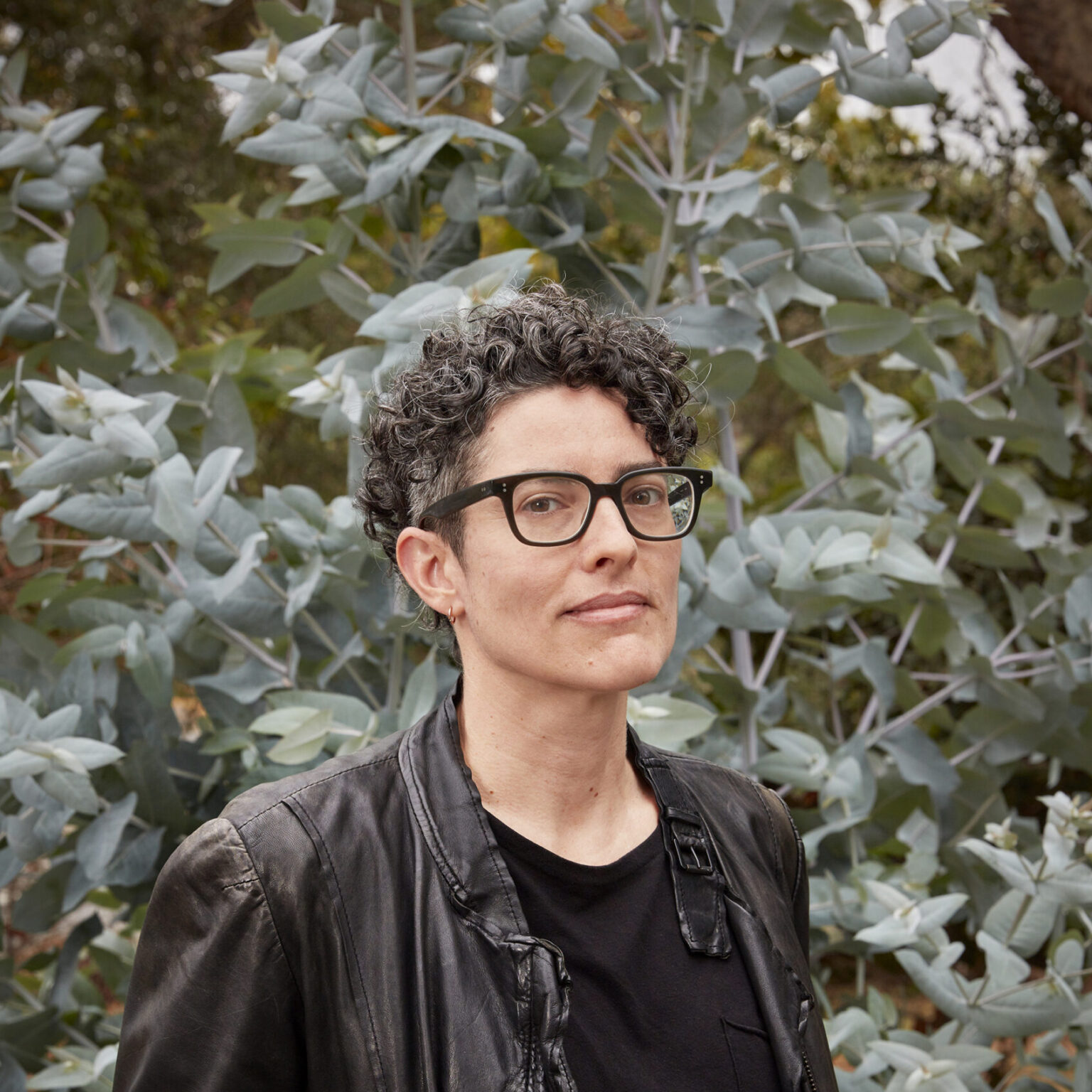 Person standing against backdrop of foliage.