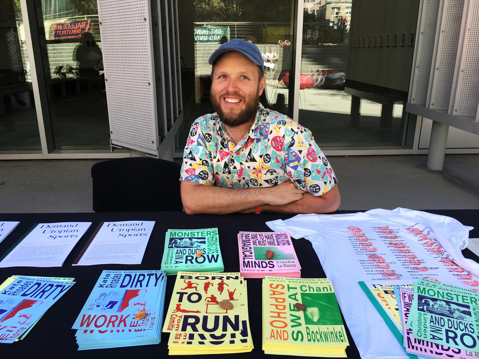 person in a colorful shirt and cap seated at a table with various print materials