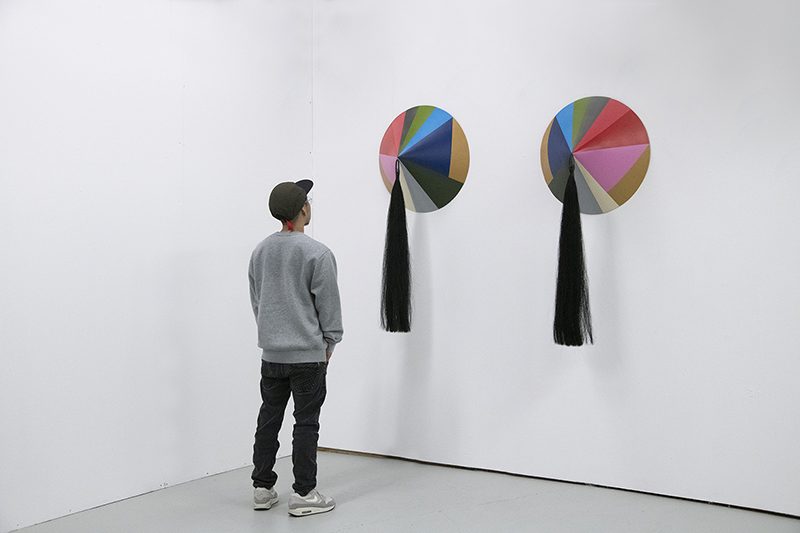 Sculpture of cones with long tassels on the wall, with figure in foreground viewing them.