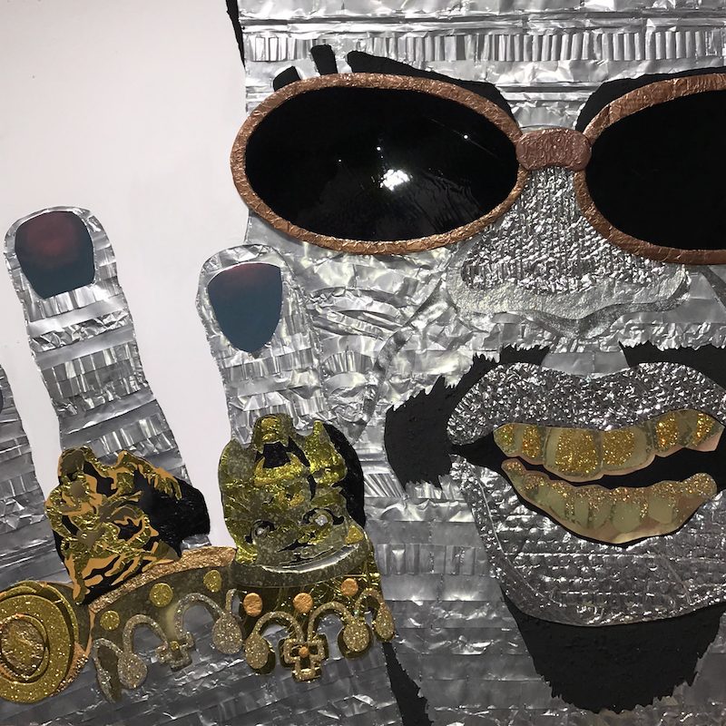 Portrait of a man with gold teeth, sunglasses, and many rings on his fingers.