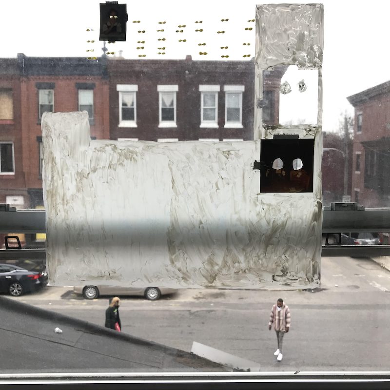 View out a window, a brick building and people passing by in background, foreground painted shapes and collage on the window glass.