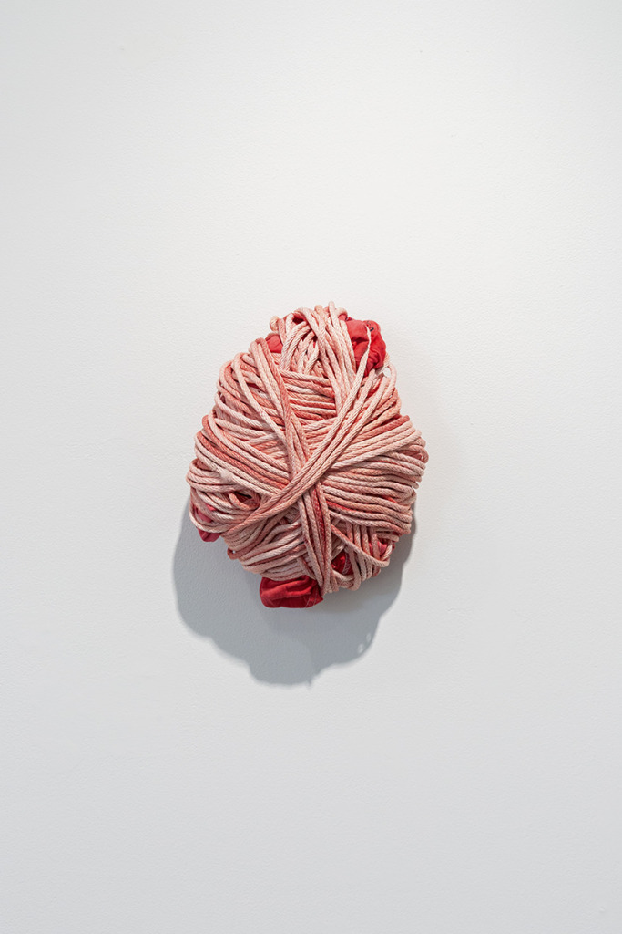 sculpture in the form of a tightly bound bundle of red cloth, mounted on the wall.