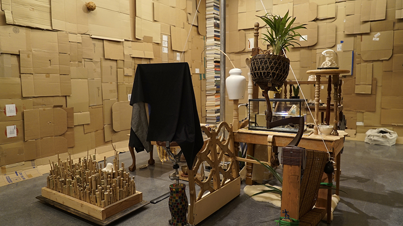 A room with various objects and furnishings, with walls covered in flattened cardboard boxes.