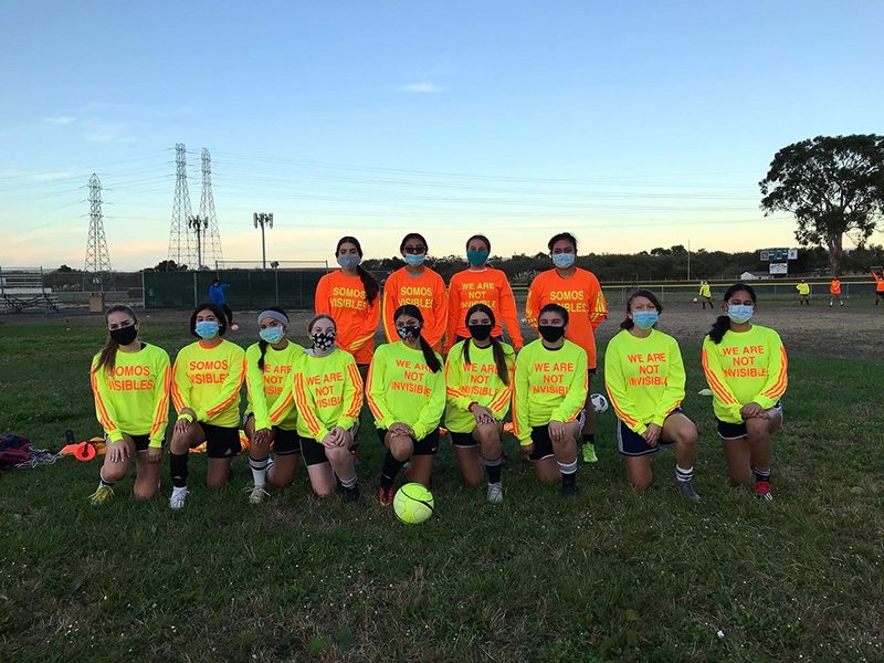 A soccer team of young people wearing bright safety orange and yellow shirts that read 