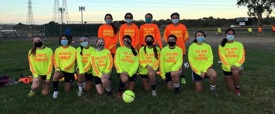 A soccer team of young people wearing bright safety orange and yellow shirts that read 