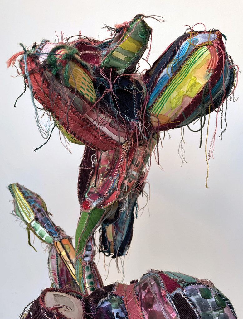 A colorful sculpture resembling a plant or cactus form, with colorful thread hanging off of it.