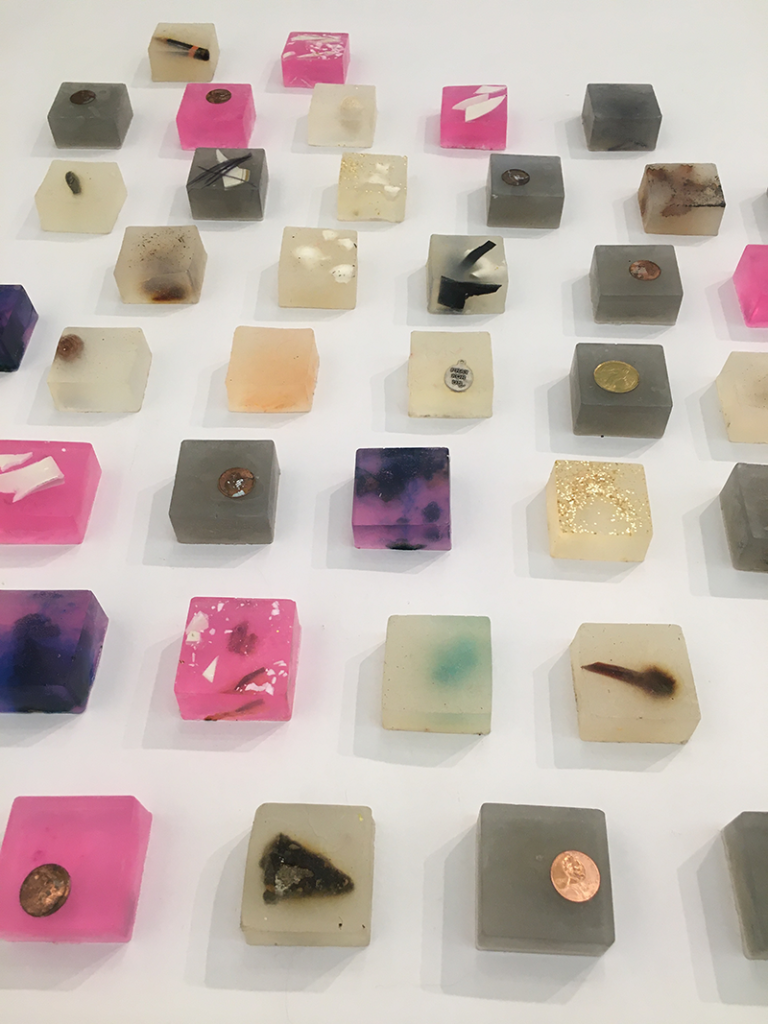Translucent blocks in hues of pink, grey, lavender, and ivory, with objects embedded inside.